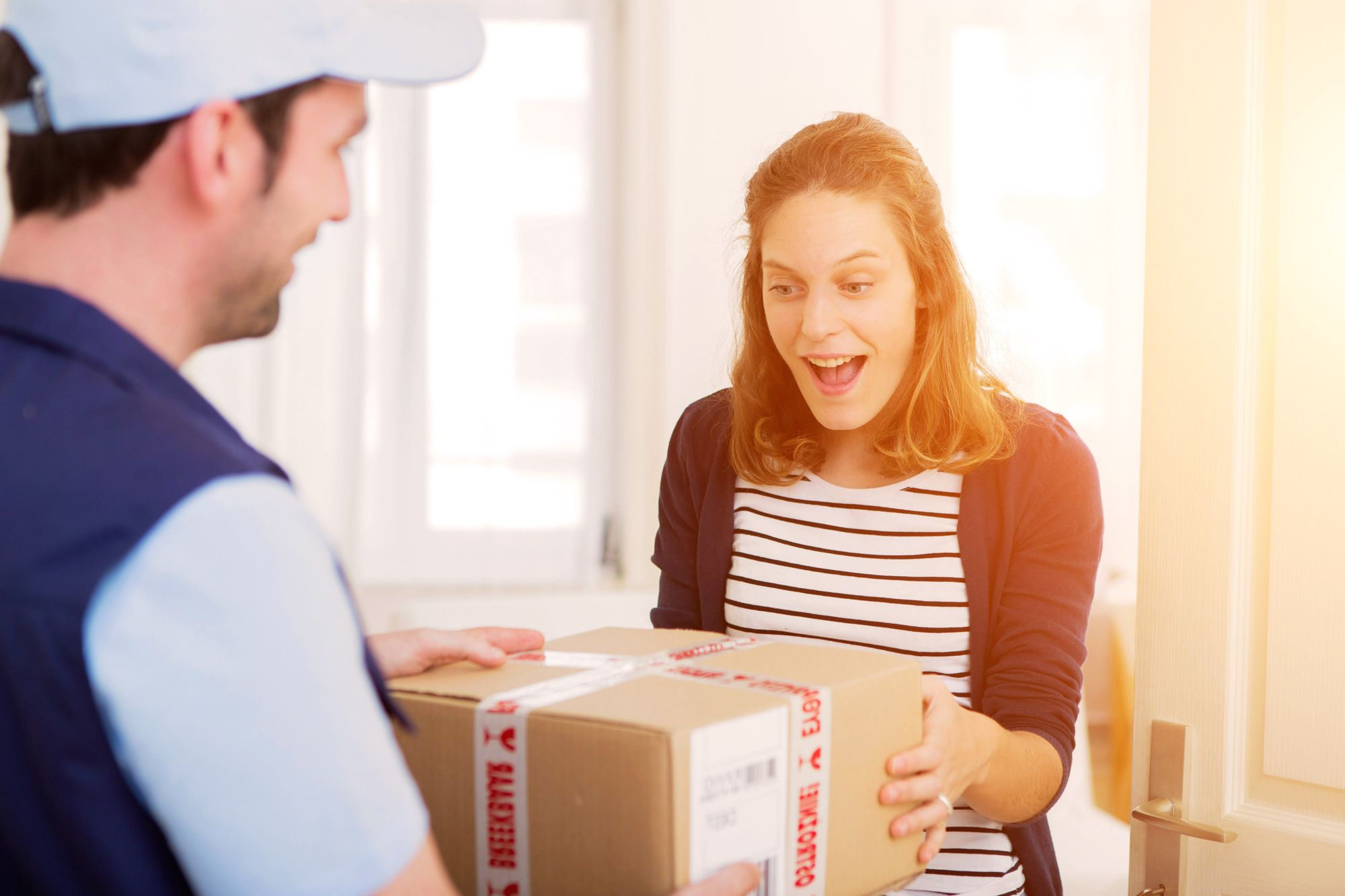 A smiling woman accepting a parcel from a delivery driver at the front door