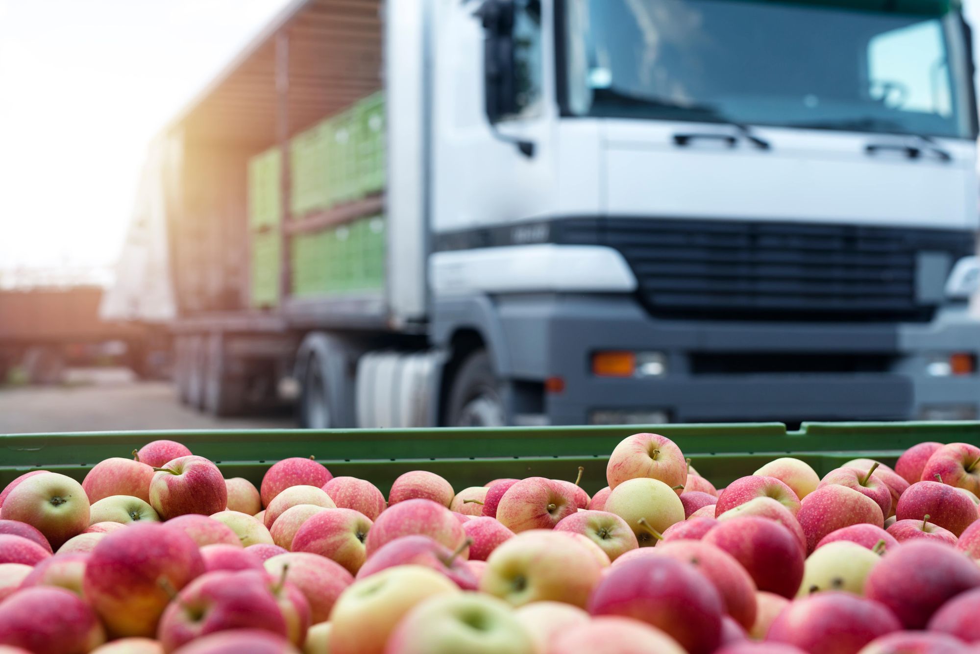 A truck in the background of a pallet of apples