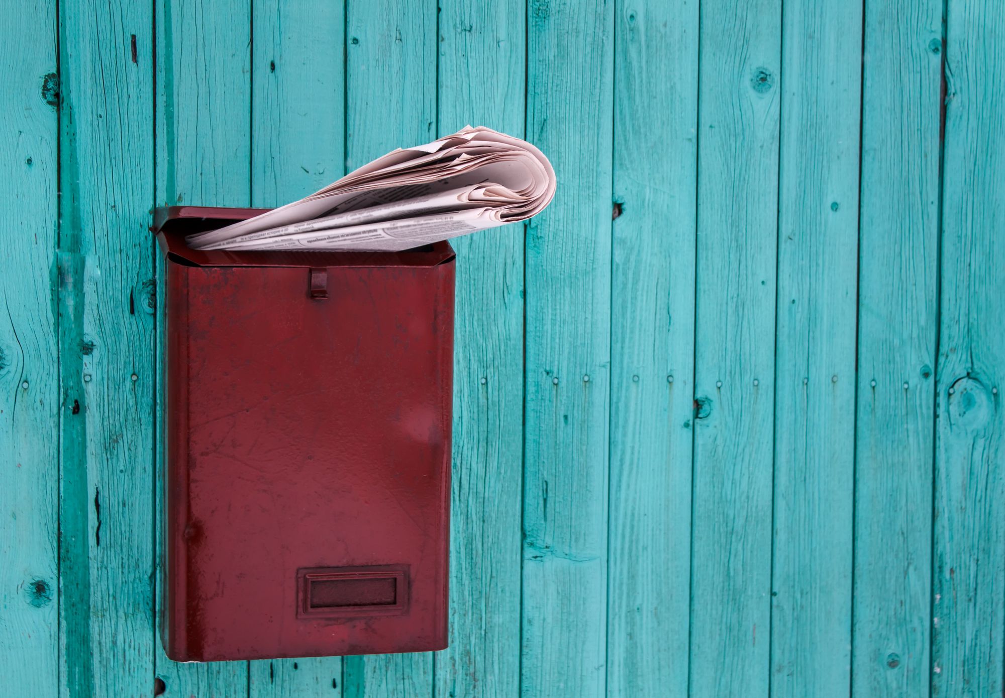 A newspaper in a red postbox on a blue timber wall