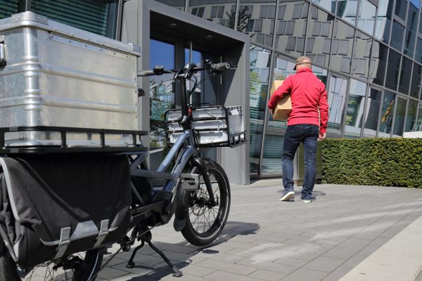 A delivery rider dropping off a parcel at an office with a cargo bike in the foreground 
