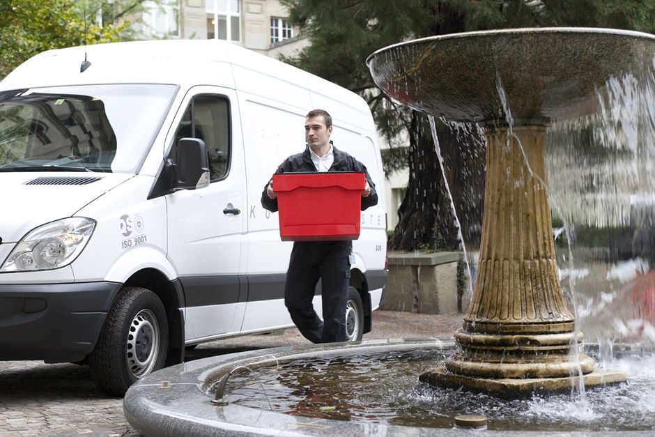 Delivery Van and driver carrying a red box walking behind a fountain